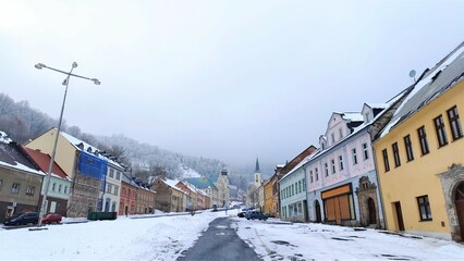 Fototapeta premium After the snowfall, snow lies on city streets and on the roofs of churches and other buildings. The roadway has been cleared by utilities for normal traffic flow. There is frost on the trees. Foggy