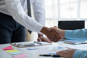 Two young Asian businessmen shaking hands and agreeing to invest in a real estate joint venture at the office.