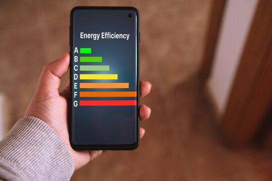 Woman's hand holds a smartphone with a Energy efficiency rating labels on screen. Low consumption and efficient products. Reduce carbon footprint. Green eco-friendly business. Low CO2 emissions.