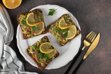 Homemade Guacamole sandwiches garnished with lemon on white plate on brown table