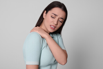 Young woman suffering from pain in shoulder on light grey background. Arthritis symptoms