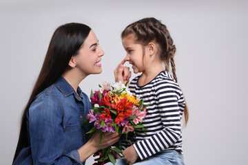 Fototapeta na wymiar Happy woman with her cute daughter and bouquet of beautiful flowers on light grey background. Mother's day celebration