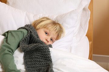 Sick boy with scarf around neck lying in bed indoors