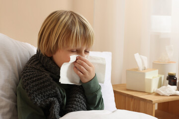 Boy blowing nose in tissue in bed at home. Cold symptoms