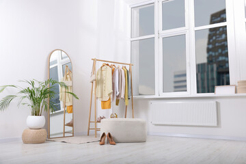 Stylish dressing room interior with mirror, ottoman and clothing rack