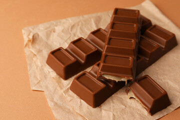 Parchment with delicious chocolate bars on light brown background, closeup