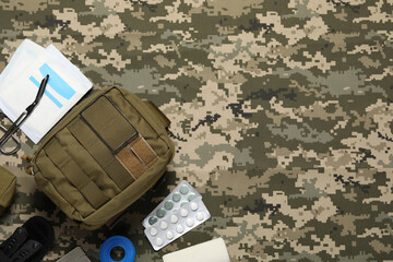 Flat lay composition with military first aid kit on camouflage fabric. Space for text