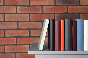 Many different hardcover books on grey table near brick wall. Space for text