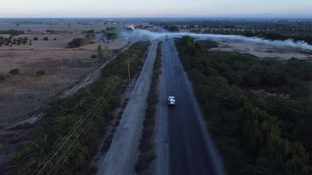 Aerial drone following shot over a car moving along RCD road with white visible in distance along rural countryside during evening time.