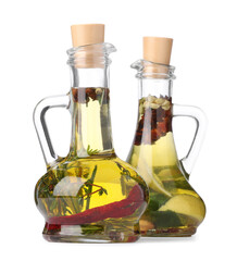 Glass jugs of cooking oils with spices and herbs on white background
