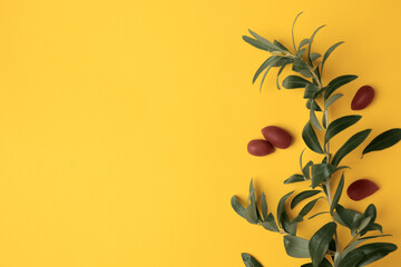Fresh olives and green leaves on yellow background, flat lay. Space for text