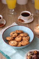 Plate of chocolate pralines, bowl of cookies, cups of tea, glasses of juice and lit candles on the table. Selective focus.