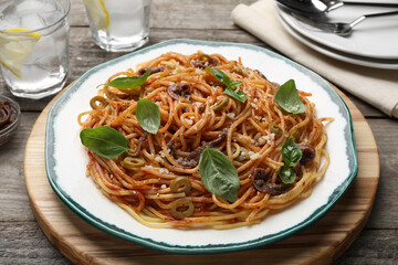 Delicious pasta with anchovies, tomato sauce and basil on wooden table