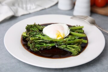 Tasty cooked broccolini with poached egg and sauce on grey table, closeup
