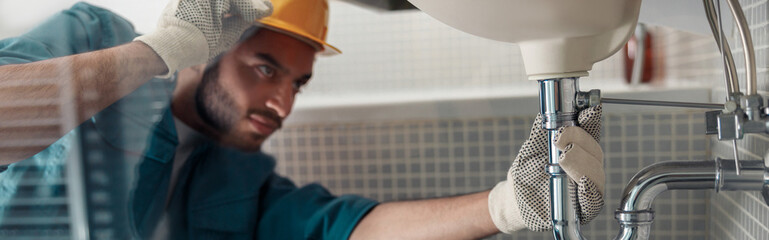 Handyman is repairing faucet of a sink at bathroom. Maintenance and household assistance concept