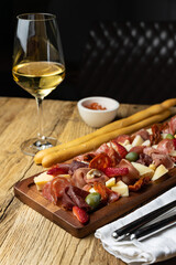 A glass of white wine sits on a table with a platter of meat cheese