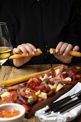 A glass of white wine sits on a table with a platter of meat cheese