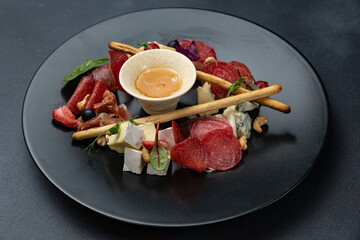A glass of white wine sits on a table with a platter of meat cheese