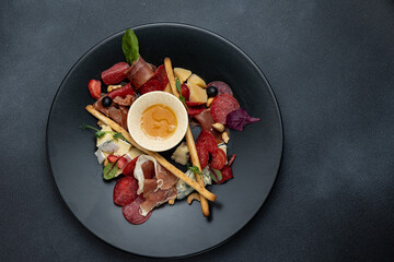 A glass of white wine sits on a table with a platter of meat cheese