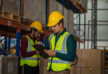 Warehouse employees using digital tablet computer for checking stock in a large distribution warehouse.