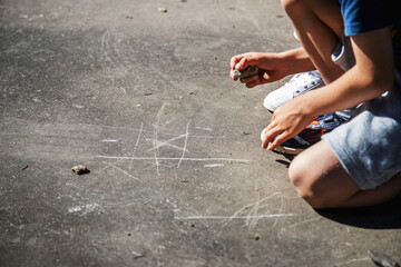 Happy childhood. Caucasian children playing outside during the day, scratching the ground with a rock to play the classic game of tic-tac-toe. Copy space