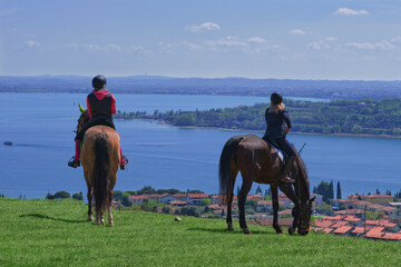 Two woman riding a horse on a hill looking into the distance rear view. Two woman on a horse looks...