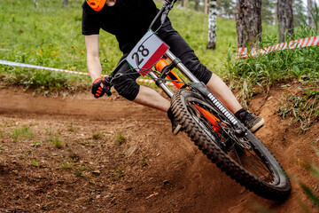 male racer athlete riding cornering turn downhill race, close-up front wheel mountain bike