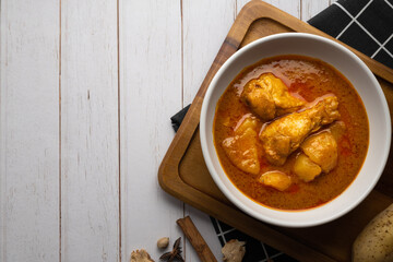 Chicken massaman with potato in white bowl on wooden table.