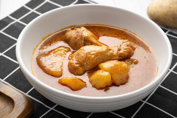 Chicken massaman with potato in white bowl on wooden table.