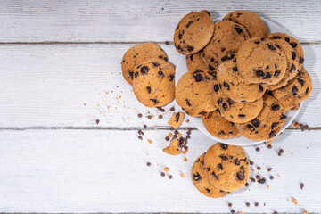Stack and plate of chocolate chips cookies. Traditional american chocolate drops crisp cookies on white wooden background, copy space