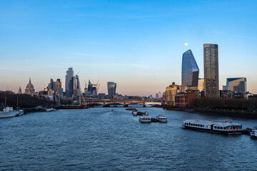 Fototapeta premium London skyline seen across the Thames at dusk with moon above skyscrapers