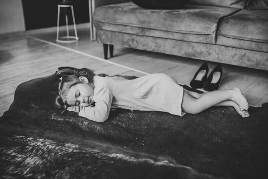 Baby sleeping in living room. Little girl is lying down on carpet on floor, she was playing, putting mother's shoes. Funny tired child falling asleep crawling on floor at home. Black and white photo.