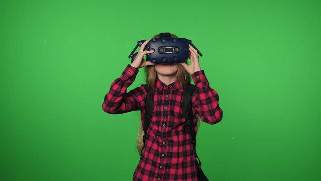 Portrait of a happy teenage girl who puts on a VR headset to play virtual reality on a green background. Chromakey.