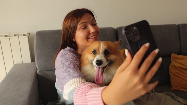 a young girl with a corgi dog and taking selfie with pet on smartphone camera. Concept stay at home, friendship with dog, taking picture. 