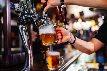 man bartender hand at beer tap pouring beer in glass in bar or pub