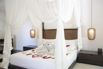 Luxury hotel bedroom interior king size bed with curtains and honeymoon decoration. Towel swans, rose flowers on the bed and happy honeymoon text