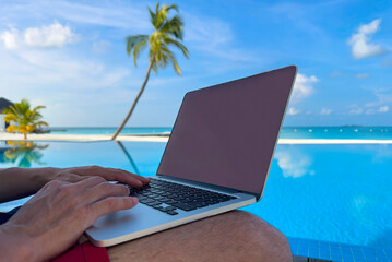 Nomad digital with laptop and running remotely with bright scenic view near poolside on the beach in summer time