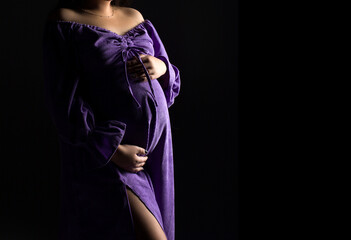 pregnancy woman in violet dress on a black background, studio pregnancy shoot
