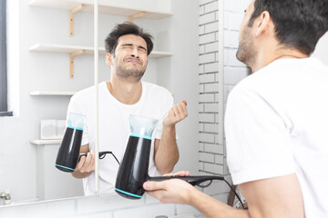 Funny man standing in front of the mirror and amusing with hair dryer in the bathroom during daily morning routine. Bad hair day concept