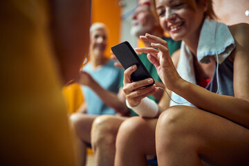 Young sporty woman using smartphone in gym locker room, setting her playlist for workout session.
