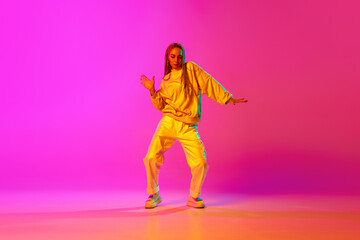 Fototapeta na wymiar Portrait with one young girl, dancer with dreadlocks dancing over gradient pink background in neon light. Contemporary dance style