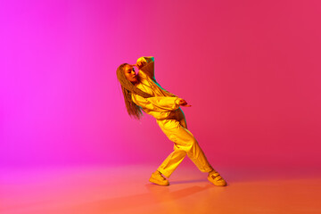 Fototapeta na wymiar Portrait with professional dancer with dreadlocks wearing hip-hop stylysh clothes and dancing over gradient pink background in neon light