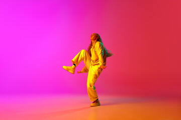 Fototapeta na wymiar Portrait with modern young dancer wearing fashion clothes in motion over gradient pink background in neon light. Funny dance