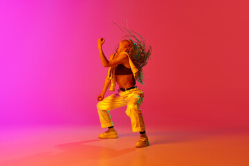 Fototapeta na wymiar One professional hip-hop dancer wearing fashion clothes moving with inspiration over gradient pink background in neon light. Contemporary choreography