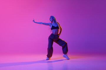 Fototapeta na wymiar Portrait with one young girl, inspired dancer with pigtails dancing with hands over gradient purple background in neon light. Hip-hop