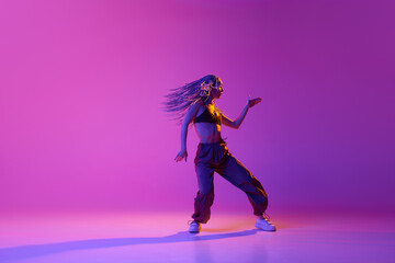 Portrait with young adorable girl with flying hair dancing over gradient purple background in neon light. Solo performance