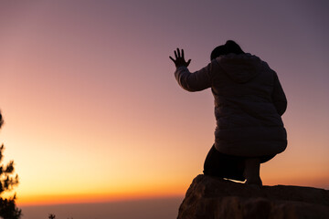 Silhouette with copy space of women hand praying or worship on top of mountain and sunrise sky abstract background. Eucharist therapy god blesses help, hope, and faith, Christian religion concept.