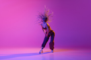 Fototapeta na wymiar Portrait with young adorable girl, dancer with flying hair dancing over gradient purple background in neon light. Solo performance