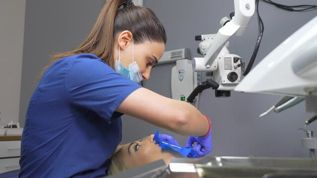 Dentist's hands in gloves with dental punch and cofferdam scarf. Dentist treats woman's tooth to patient with rubber dam. Modern dental office. Treatment elimination of caries, installation of filling