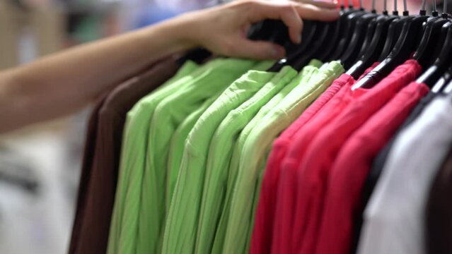 In a clothing store, close up female hands are sorting through colored shirts.